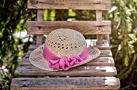 brown wicker hat with pink ribbon on top of brown wooden chair