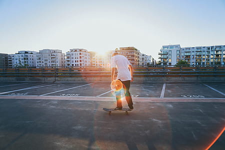 man wearing white t-shirt and black pants standing on skateboard during daytime