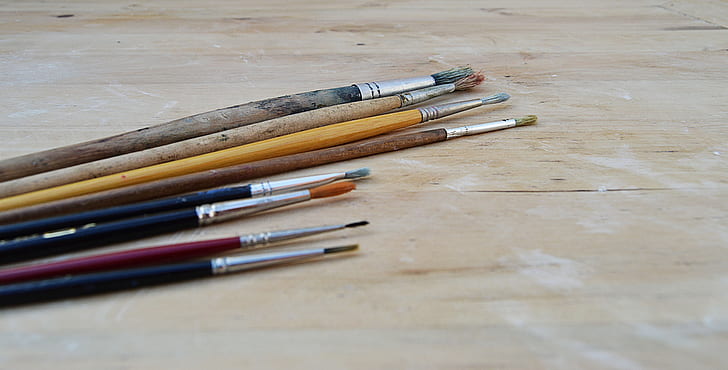 assorted-color paint brushes on brown table
