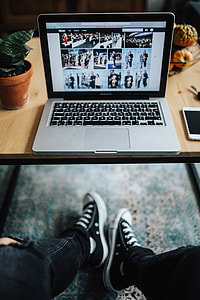 Woman in ripped jeans and black sneakers with a silver laptop on a wooden table