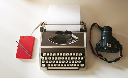 black DSLR camera; grey typewriter; red tablet computer flip case