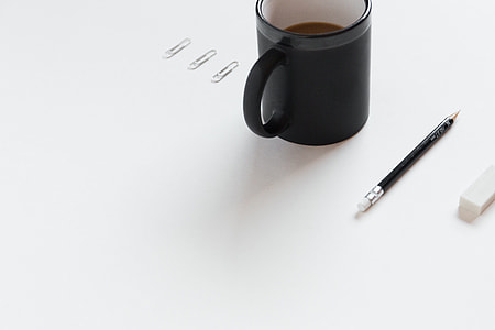 three gray paper clip beside black ceramic coffee mug and pencil on white surface close-up photo