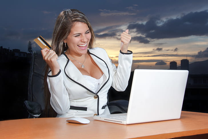 woman in white blazer holding card while looking at MacBook white