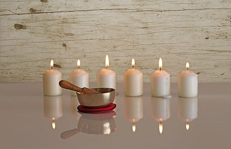 six white pillar candles behind brass-colored bowl reflecting on white surface