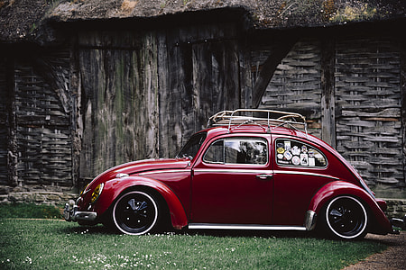 red Volkswagen Beetle parked on grass beside gray wooden cabin