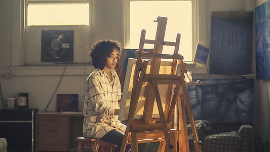 woman wearing white sport shirt painting on canvas while using easel