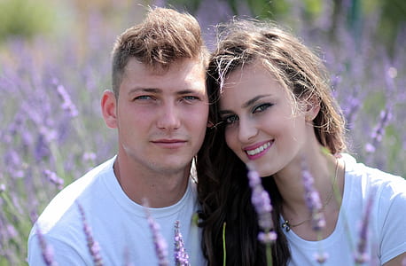 shallow focus photography of man and woman wearing white crew-neck tops surrounded by purple flowers