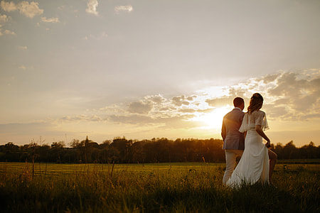 bride and groom walks on grass with sunrise background