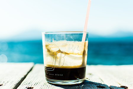clear rocks glass filled black coffee with straw on wooden dock