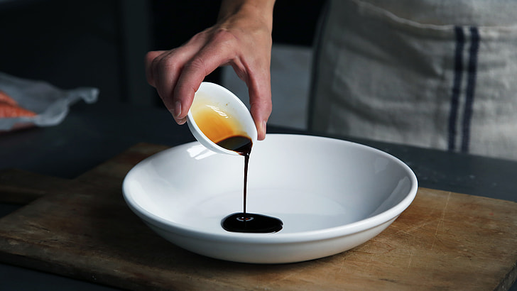 person pouring soy sauce on plate