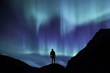 photo of person standing on mountain tops with a view of Aurora in the sky