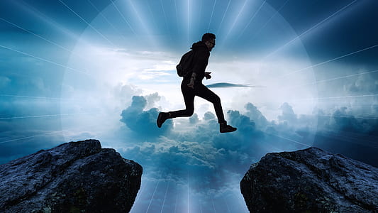 man jumping beside two rocks with background of clouds