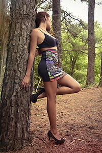woman wearing spaghetti strap crop top and mini skirt leaning on tree trunk