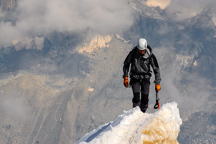 man wearing jacket walking on mountain covered in ice