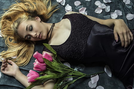 woman lying beside pink petaled flowers