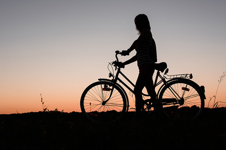 A silhouette of a woman with a bicycle at sunset