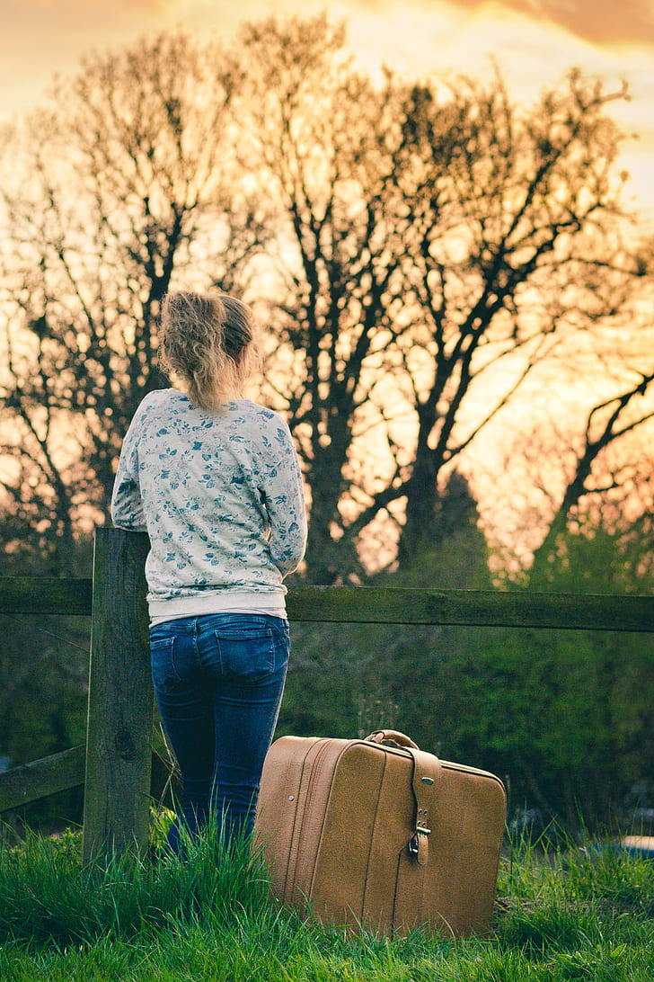 woman wearing gray long-sleeved shirt and blue jeans beside brown travel luggage