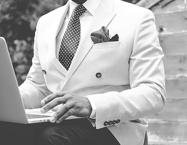 grayscale photo of man wearing white suit with laptop on lap