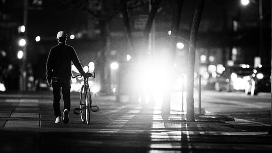 man walking beside his bike in grayscale photography