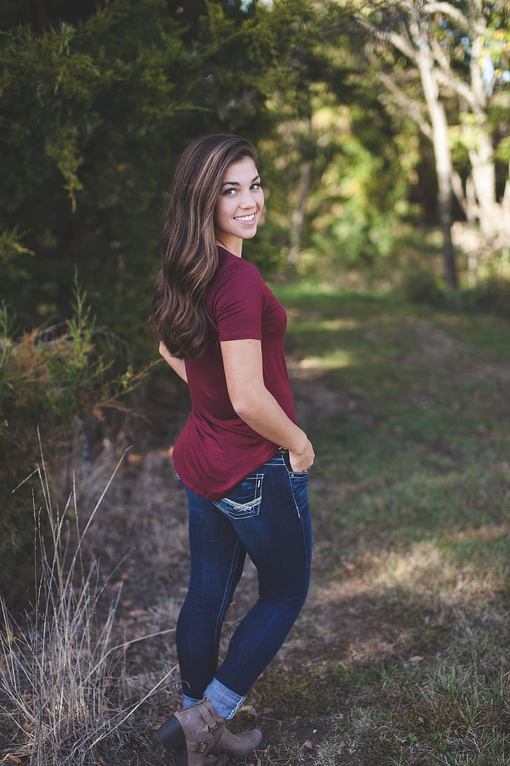 woman in maroon shirt and blue jeans standing outdoor