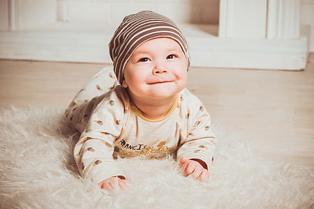 baby wearing brown sleep suit and gray knit cap in white fur floor rug