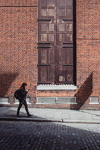 woman holding smartphone walking in front of brown bricked building