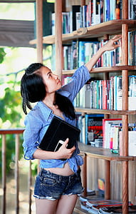 woman with blue sport shirt reaching of a book on a bookcase