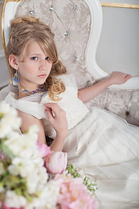 blonde haired girl wearing white dress sitting on tufted grey chair