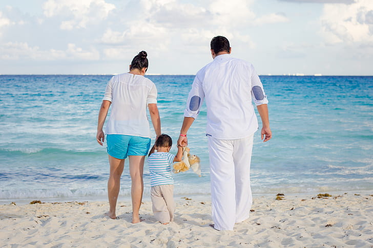 mother, father, and child walking on sea shore during daytime