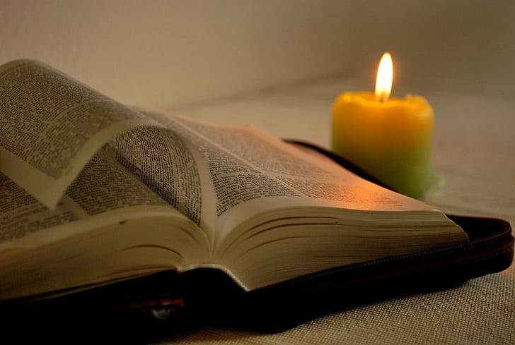 lighted yellow candle near opened book