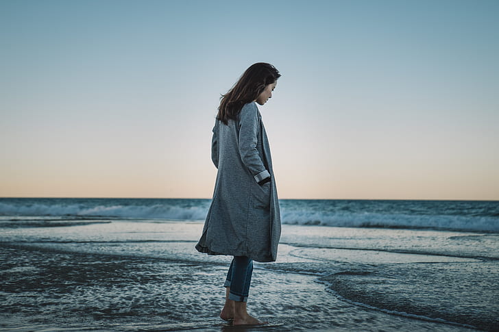 woman wearing gray coat standing on seashore
