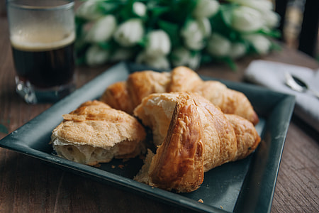 croissant on green ceramic plate beside drinking glass with coffee