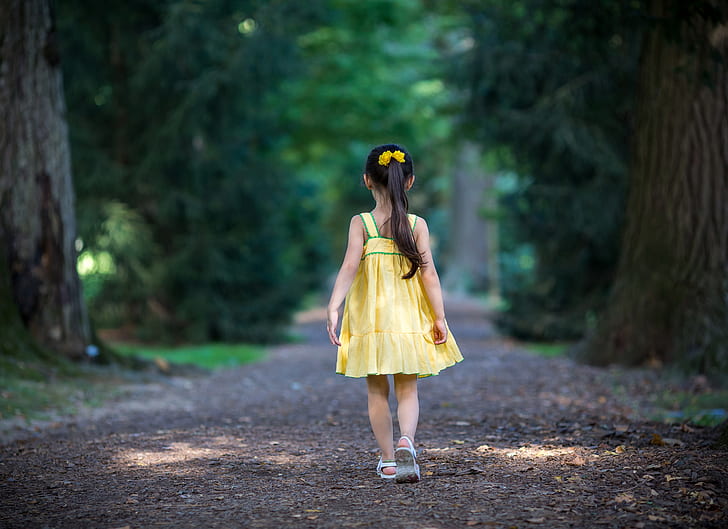girl in yellow dress standing between trees pathway