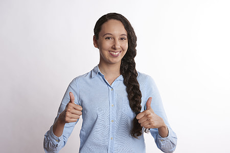 woman with braided hair wearing teal button-up dress shirt giving two thumbs up sign